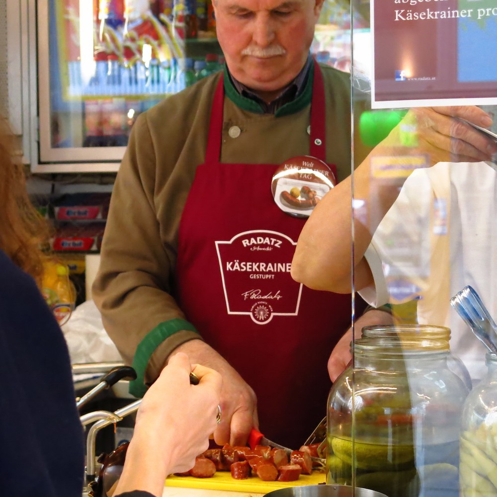 Ein Mann mit einer Radatz-Schürze schneidet eine Eitrige - einen Käsekrainer
